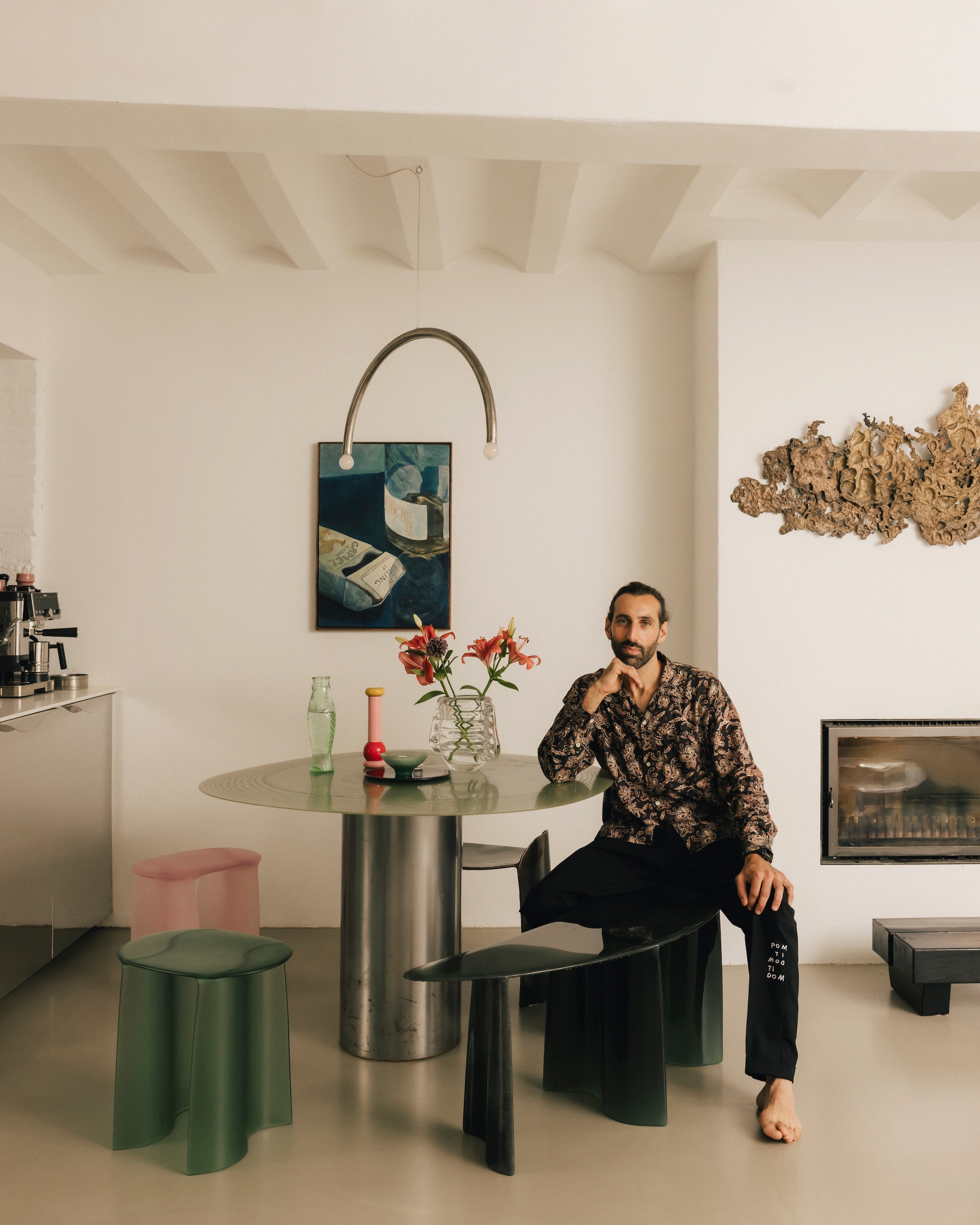Tafel Pillar Table, bankje New Wave Curved Bench en schaal Fiberglass van Lukas Cober. Kruk Calle Christian Fregnan. Pepermolen Mp0210 van Alessi. Hanglamp Rainbow van Hannah Kuhlmann. Lage houten tafel rommelmarkt. Kunstwerk links Karel Dicker. Kunstwerk erfstuk van Lukas’ oma. Betonnen vloer.