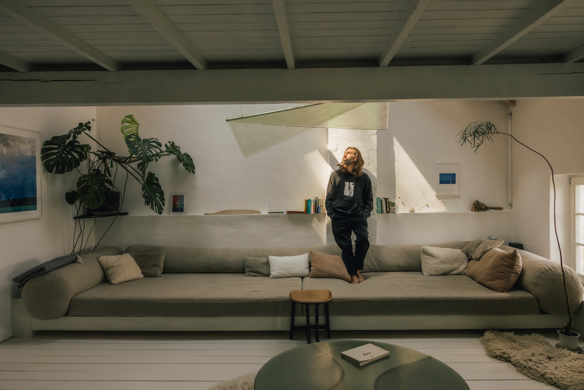 Loungebank, hanglamp en salontafel New Wave van Lukas Cober. Fotografie Jonas Loellmann. Kruk Fall/Winter van Valentin Loellmann. Plant Monstera. Originele houten plankenvloer, wit geschilderd. vtwonen design 8-2026 | Fotografie Katoo Peeters