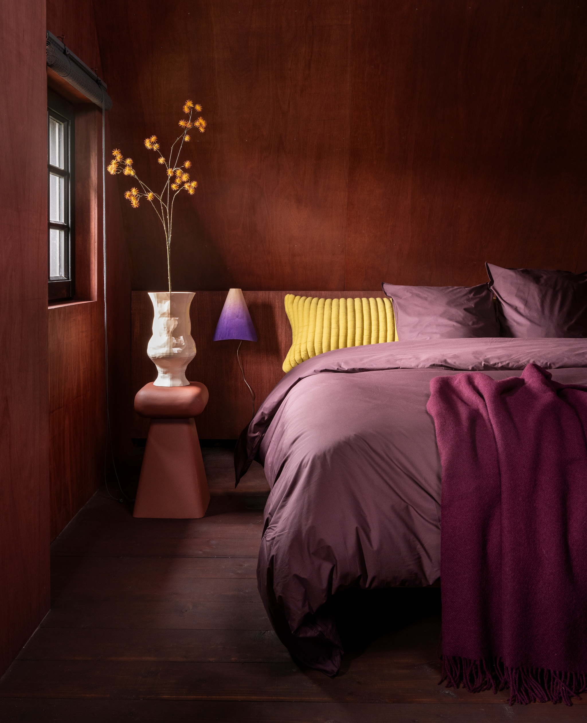 Suite 702 dekbedovertrekset, katoen, plum noir € 117,90, kussensloop, katoen, plum noir € 22,95, bedmate, dons, wit € 114,95, bedmatesloop, katoen, geel € 55,- (suite702.com). Zuiver kruk Earth, ijzer, terracotta € 119,- (shop.vtwonen.nl). Ralf Gloudemans vaas Caldra, aardewerk, roze dégradé € 272,- (cor-unum.nl). Onno Adriaanse muurlamp Dawn, hout, paars dégradé € 175,- (onnoadriaanse.nl). Aabe plaid Boston 412, lamswol, paars € 135,- (aabe.nl). Wand afgewerkt met Linolie lijnzaadolie, satin wood oil rom, rood, prijs op aanvraag (linolie.dk). vtwonen 10-2026 | styling Marianne Luning | fotografie Stan Koolen