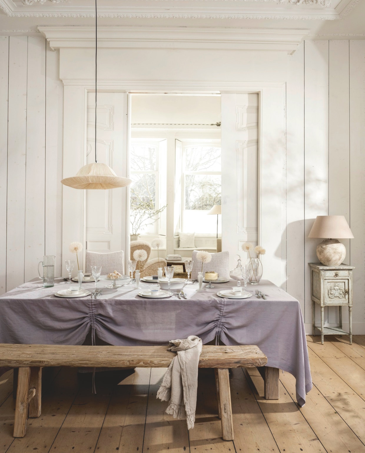 Het Kabinet Oude Chinese eettafel, iepenhout, 225x99x76 cm (lxbxh) € 2295,-, Oude Chinese bank, iepenhout, 181x27x50 cm (lxbxh) € 459,- (hetkabinet.nl). Rivièra Maison eetkamerstoelen Monti, katoen, viscose, linnen en rubberhout, antique white, 50x67x100 cm (bxdxh) € 349,- (cejorwonen.nl). Zara Home tafellamp, aardewerk, bruin € 179,-, vaas met geschulpte rand, glas € 29,99, gegraveerde wijnglazen, kristallook € 7,99, vierdelige bestekset, staal € 35,99, Colin King kandelaar (als vaas), matglas € 29,99, naamkaarthouders en kaartjes, metaal en papier, set van 8 houders en 24 kaartjes € 15,99 (zarahome.com). By-boo hanglamp Lokta 2, handgeschept papier, wit, 62,5x19,5 cm (Øxh) € 189,- (by-boo.com). Piet Jonker antiek Frans nachtkastje, hout, grijs patina, 38,5x38x83 cm (lxbxh), prijs op aanvraag (pietjonker.nl). Urban Nature Culture schenkkan, gehamerd glas € 39,99 (shop.vtwonen.nl). Taartschalen, glas (kringloop). Oury Home tafelkleed met trekkoordplooien, linnen, lila, 320x200 cm (lxb) € 325,- (ouryhome.com). Serax serviesgoed, collectie Silhouette Dinnerware, porselein, wit, vanaf € 5,-, bonbonnière, collectie The Josephine, glas € 95,- (serax.com). Kims Home Luxury geprepareerde paardenbloemen € 18,95 (kimshomeluxury.nl). vtwonen Landelijk 06-2026 | styling Kim van Rossenberg | fotografie Stan Koolen