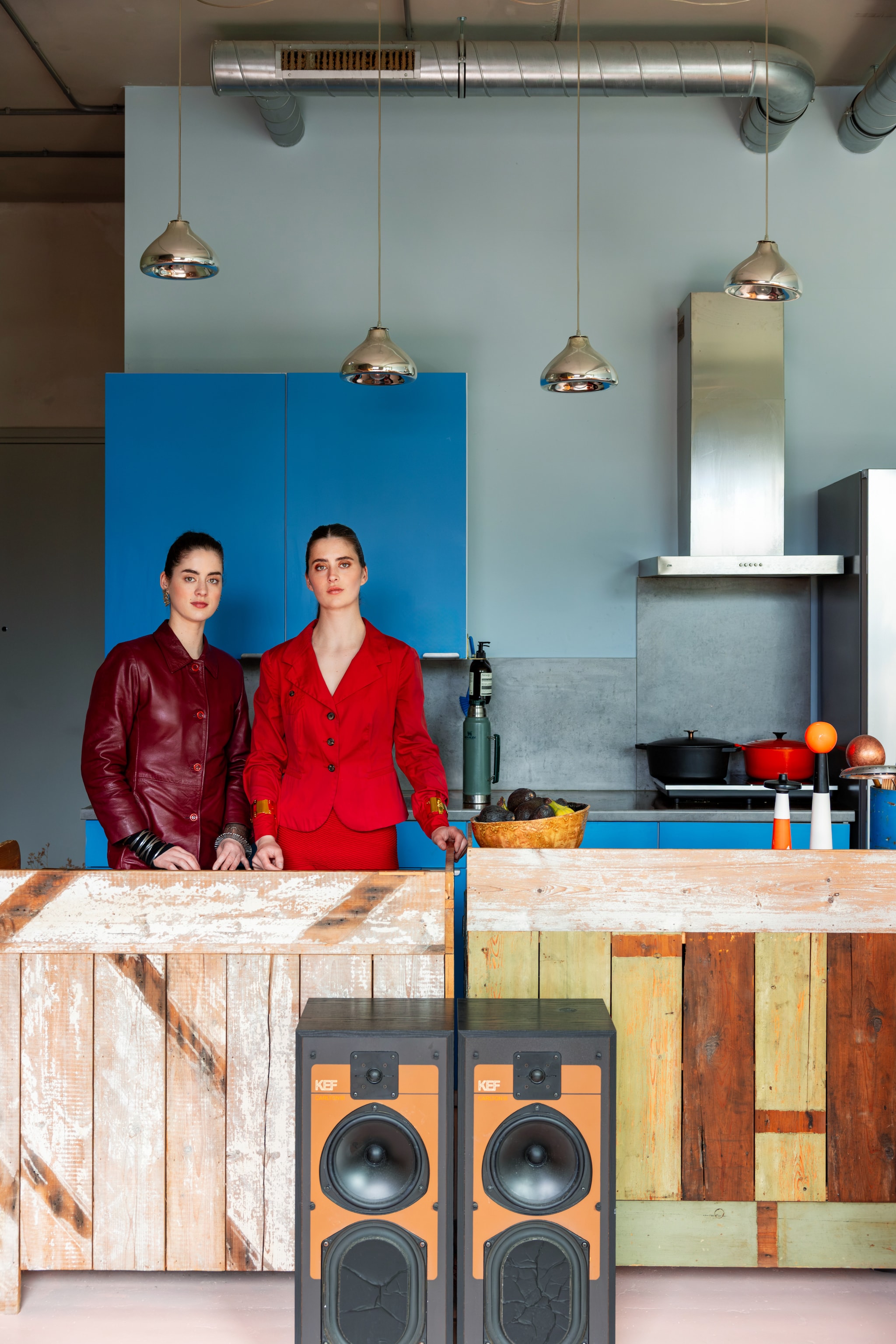 Geertje (links) en Roos in de loft van Roos. Muurverf zelf gemengd, keukenfronten zelf gezaagd en geverfd. Houten eiland Piet Hein Eek. Hanglamp en oranje objecten Tom Dixon. Geluidsboxen Kef. Pannen Le Creuset. Schaal vintage.
