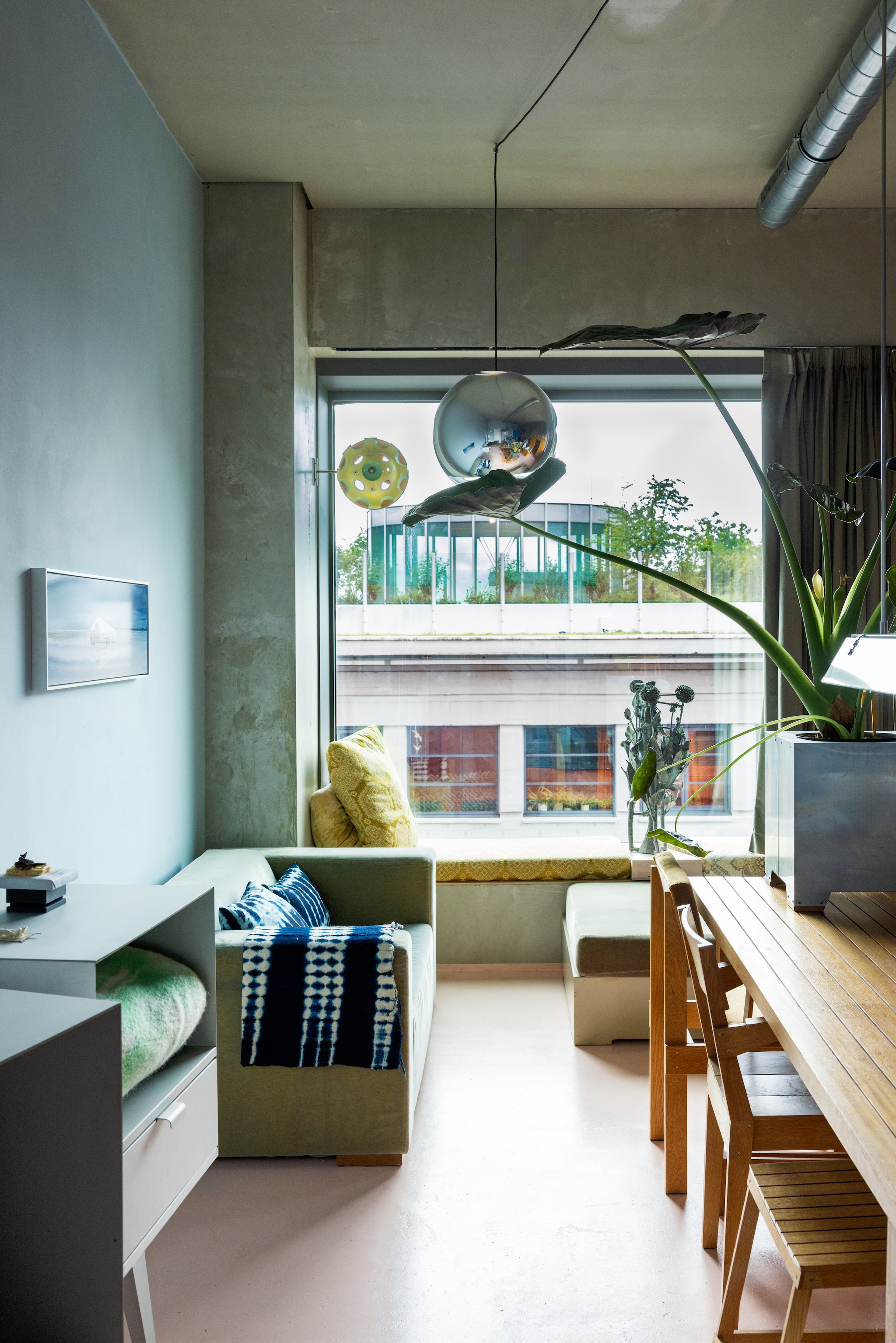 Muur van beton. Keukeneiland met koperen aanrecht en blauw gelakte kasten. Kruk Piet Hein Eek. Spatelpot zelfgemaakt van afgezaagde buis. Schaal en karaf vintage. vtwonen 10-2026 | styling Djolien De Kreij | fotografie Dana van Leeuwen