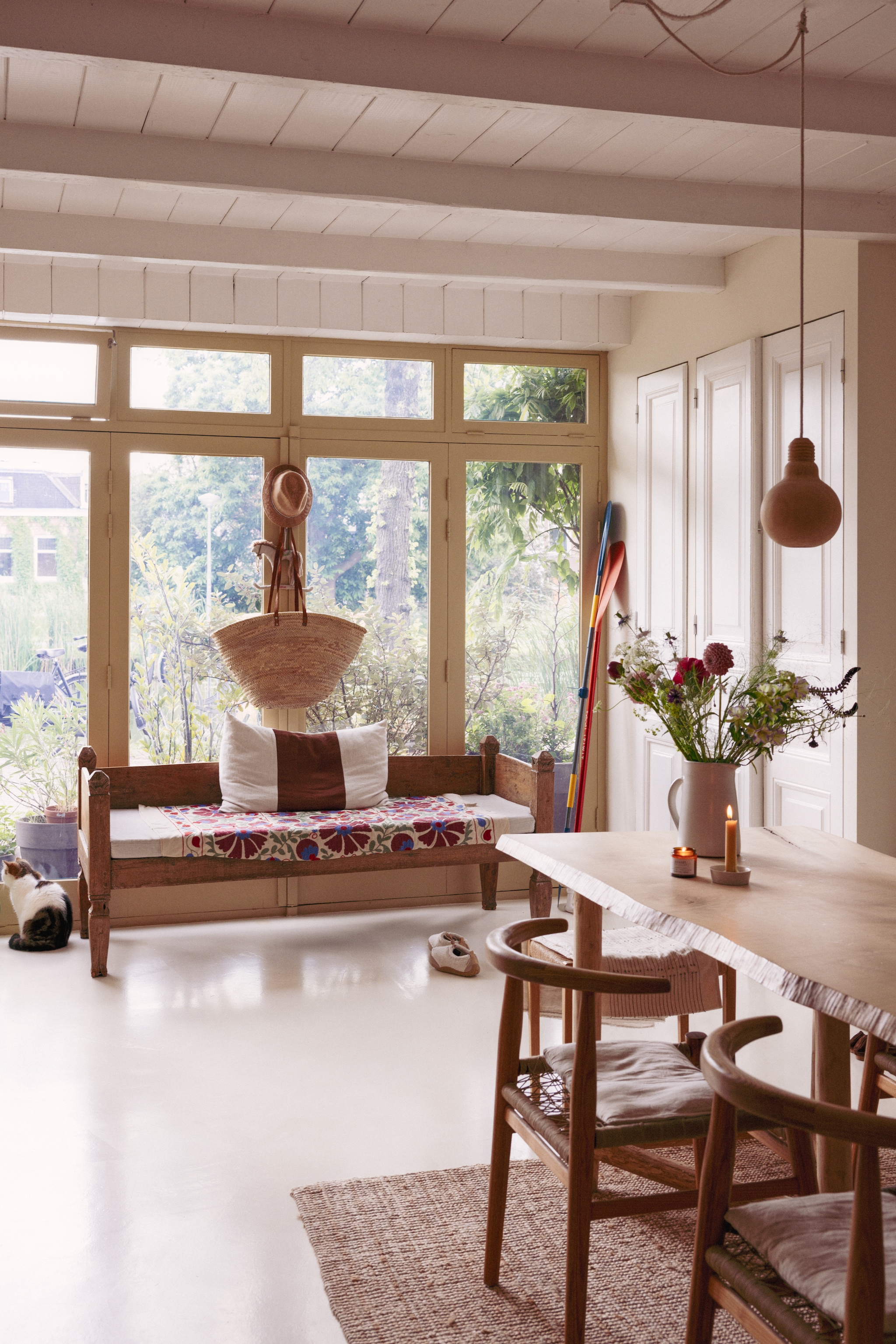 Cementvloer kleur White Tie, muur kleur School House White, en kasten en plafond kleur All White van Farrow & Ball. Bank uit Indonesië. Plaid Khasto. Kussens Fant. Kruik en servies Atelier Sukha. Tafel gemaakt door Lumineus. Stoelen Vogel Design. Kruk Atelier Mooijen. Vloerkleed Ikea. Lampen From Africa With Love. Hoed Pomandere.