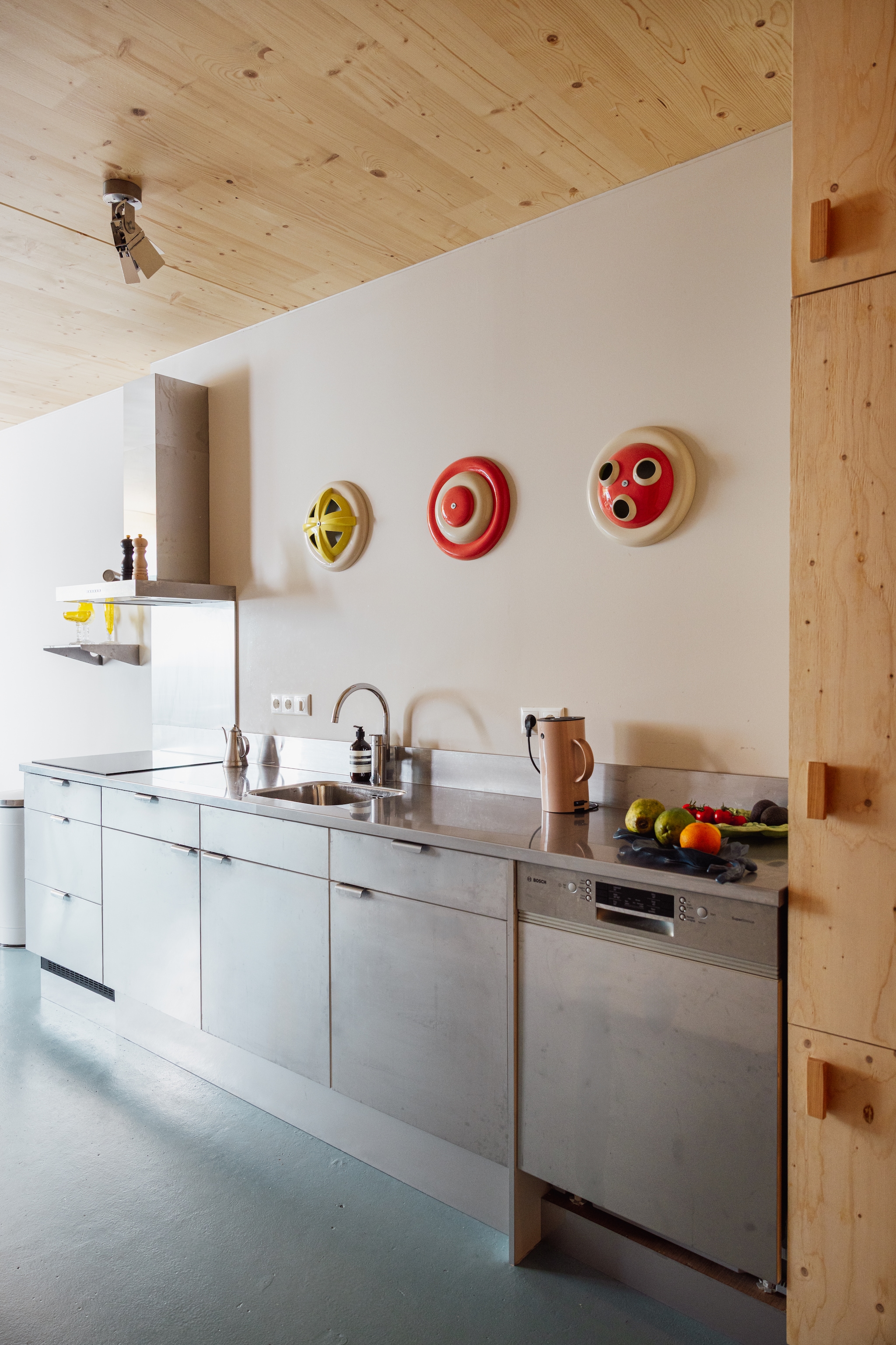 Vloer Paulycote kleur Sikkens Q8.15.55. Keuken afgewerkt met rvs. Wandobjecten Jeanine Eek-Keizer. Plafondspot Piet Hein Eek. Waterkoker Stelton. Peper- en zoutstel Le Creuset. Gieter Sekelskifte. vtwonen 10-2026 | styling Djolien De Kreij | fotografie Dana van Leeuwen