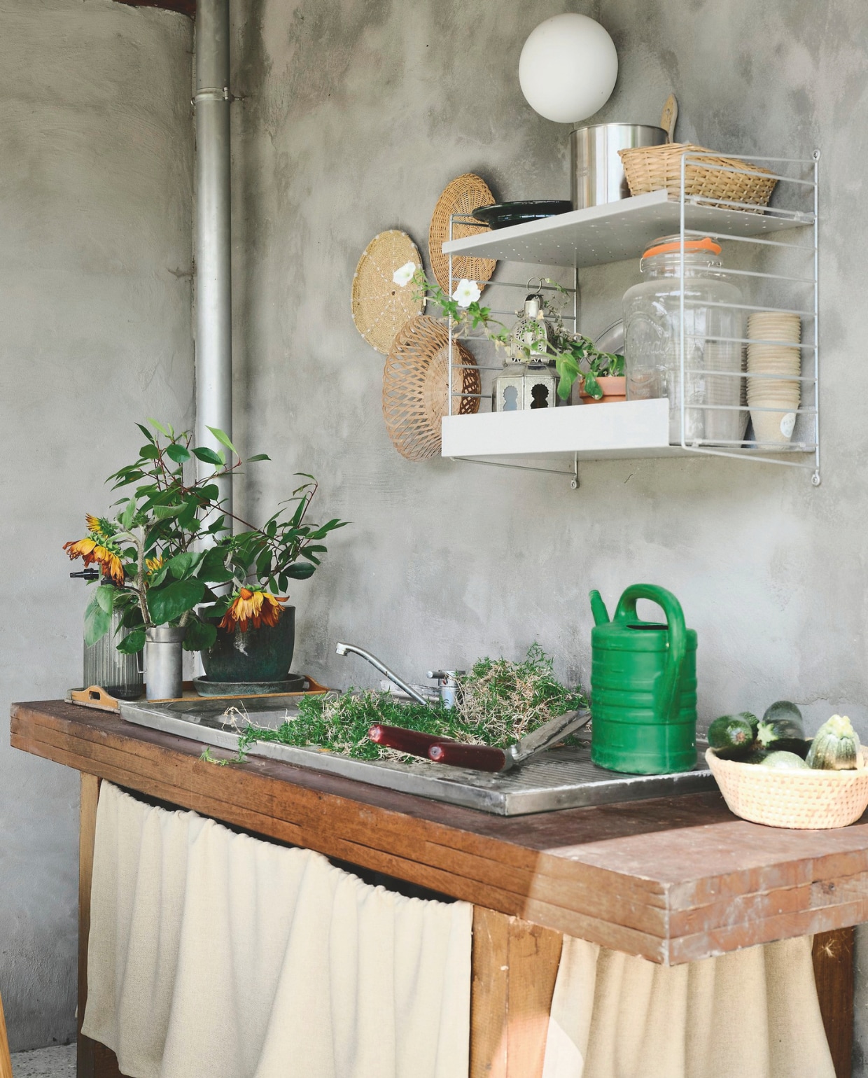 Buitenkeuken gemaakt van een oude tafel en keukenwastafel. Metalen wandrek String Furniture. Muurlamp Flos. Rotan manden vintage. vtwonen 08-2026 | fotografie Mr. Frank