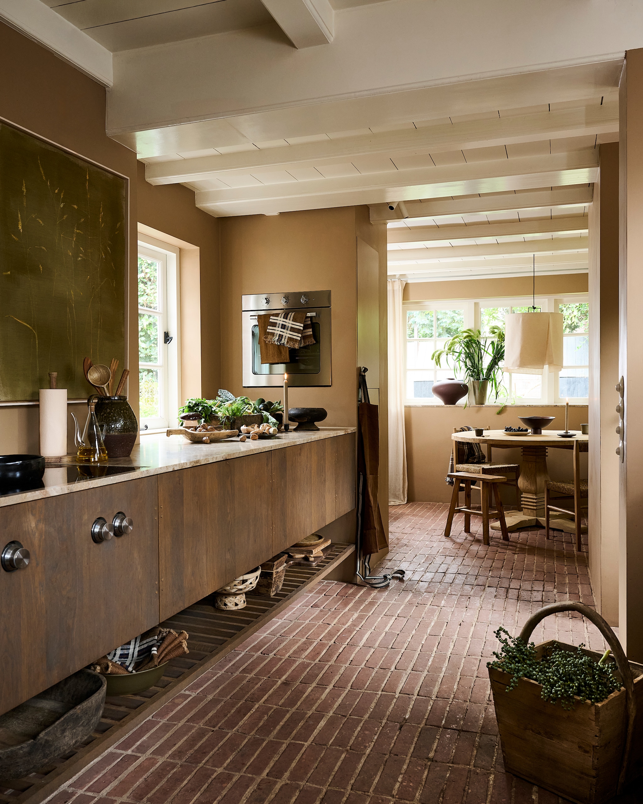 Lab muurverf, velvet fudge, 1 liter € 60,- (labcolourtheworld.com). Keuken met brechia di nola marmeren blad, ontwerp van bewoonster Maaike Schmeets (instagram.com/studioheiligland). Ikea oven (ikea.com). Schilderij Grassen op mosgroen € 1100,- (maartjevandennoort.nl). Zara Home keukenrolhouder € 15,99, kandelaar € 15,99, eetkamerstoel € 189,-, karaf € 17,99 (zarahome.com). Toni Copenhagen kraan SP Tap on Standpipes, S200, nikkel (tonicopenhagen.com). vtwonen pot, keramiek, groenbruin € 89,95, Urban Nature Culture schaal Orion op voet, hout, bruin € 149,99, vaas Nomsa op vensterbank, bruin € 149,99 (shop.vtwonen.nl). Madam Stoltz slacouvert, olijfhout € 14,50, pollepels, hout en bamboe, set van 2 € 27,50 (madamstoltz.dk). Luksa Home Collection schep, hout € 59,95, trog, hout € 179,-, schaal op voet, hout € 74,95, bak met handvat op grond, hout € 89,95, kruk € 89,95, eettafel, 150 cm (Ø) € 1199,- (luksa.furniture). Libeco theedoeken, linnen, vanaf € 24,-, schort, linnen  € 164,-, placemats, linnen, vanaf € 24,- (libeco.com). Ro Smit mok € 9,95, ontbijtbord € 21,94 (rosmit.nl). Op plank onder keukenkasten: Luksa Home Collection schaal, hout, zwart € 79,95, vierkante bakken, hout € 34,95 (luksa.furniture). Ro Smit schaal, aardewerk, groen € 98,- (rosmit.nl). Arket mand op poot, bamboe € 35,99 (arket.com). Overig privébezit.