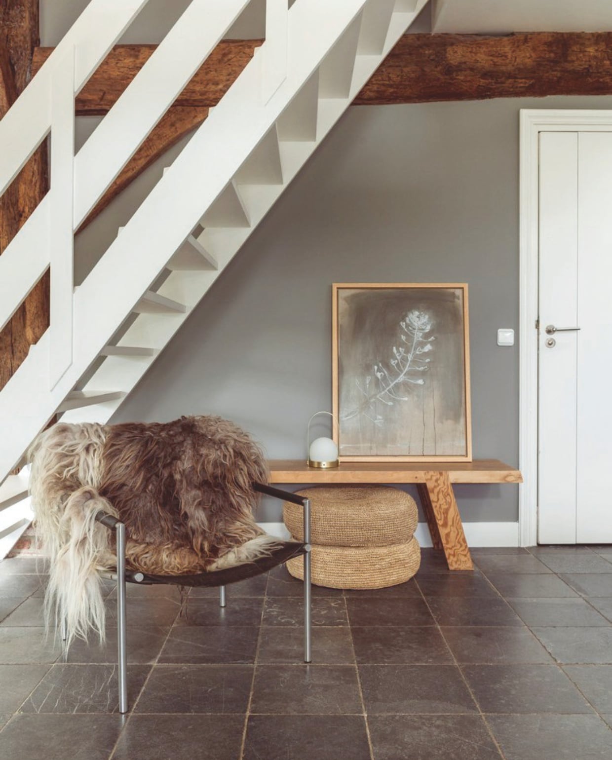 Schilderij Gea Slotman. Houten bank maatwerk Roel Westerman. Rotan poefs Anne-Marie Wonen. Leren stoel vintage. Schapenvacht Studio Hebbe!. vtwonen Landelijk 7-2026 | fotografie Suzanne Paap