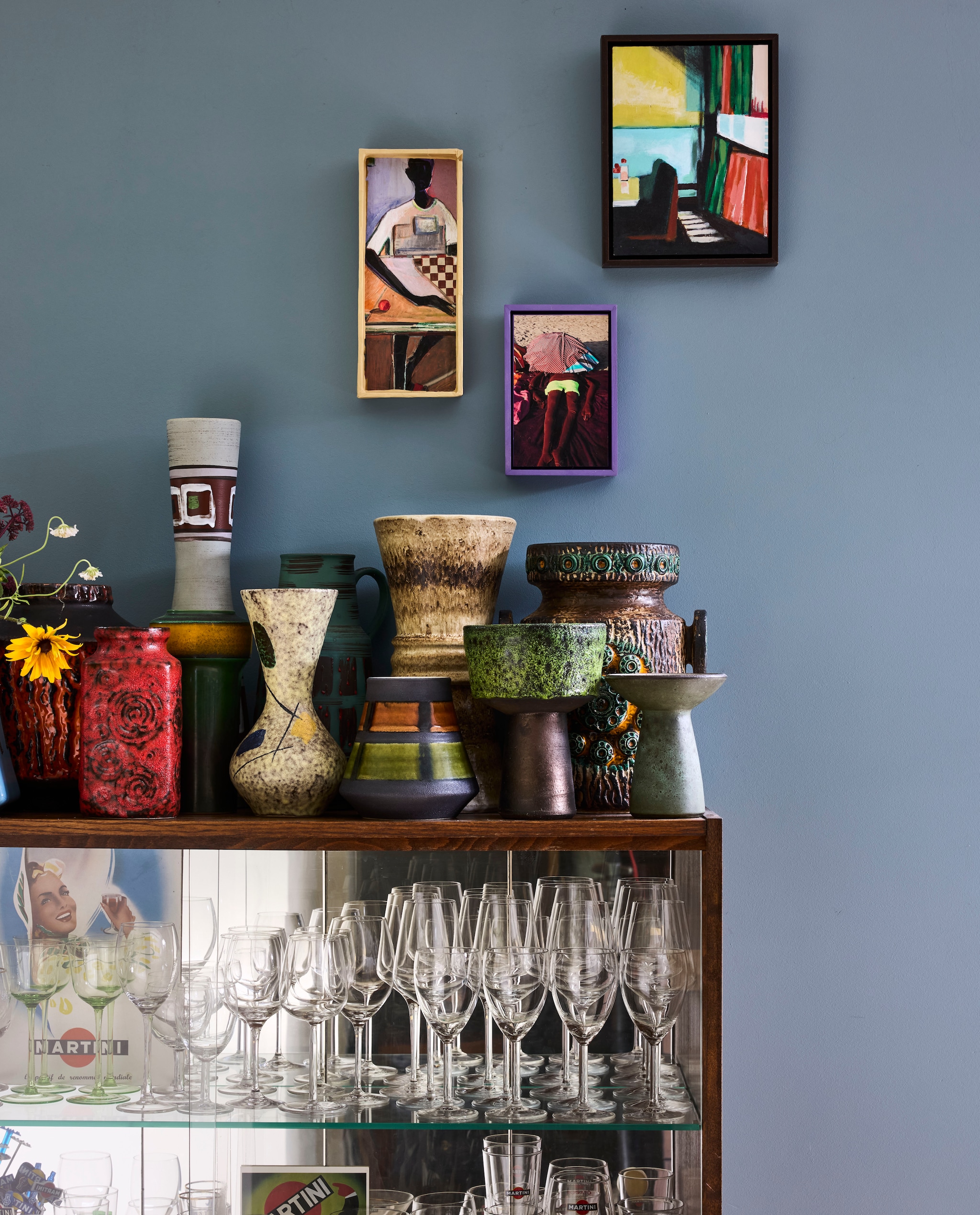 Verzameling West-Duitse lavavazen. Glazen kast Van Dijk & Ko. Schilderij rechts Monique de Ruijter. Schilderij links Frank Visser. Foto Mirjam Bleeker. vtwonen 10-2026 | styling Fietje Bruijn | fotografie Alexander van Berge