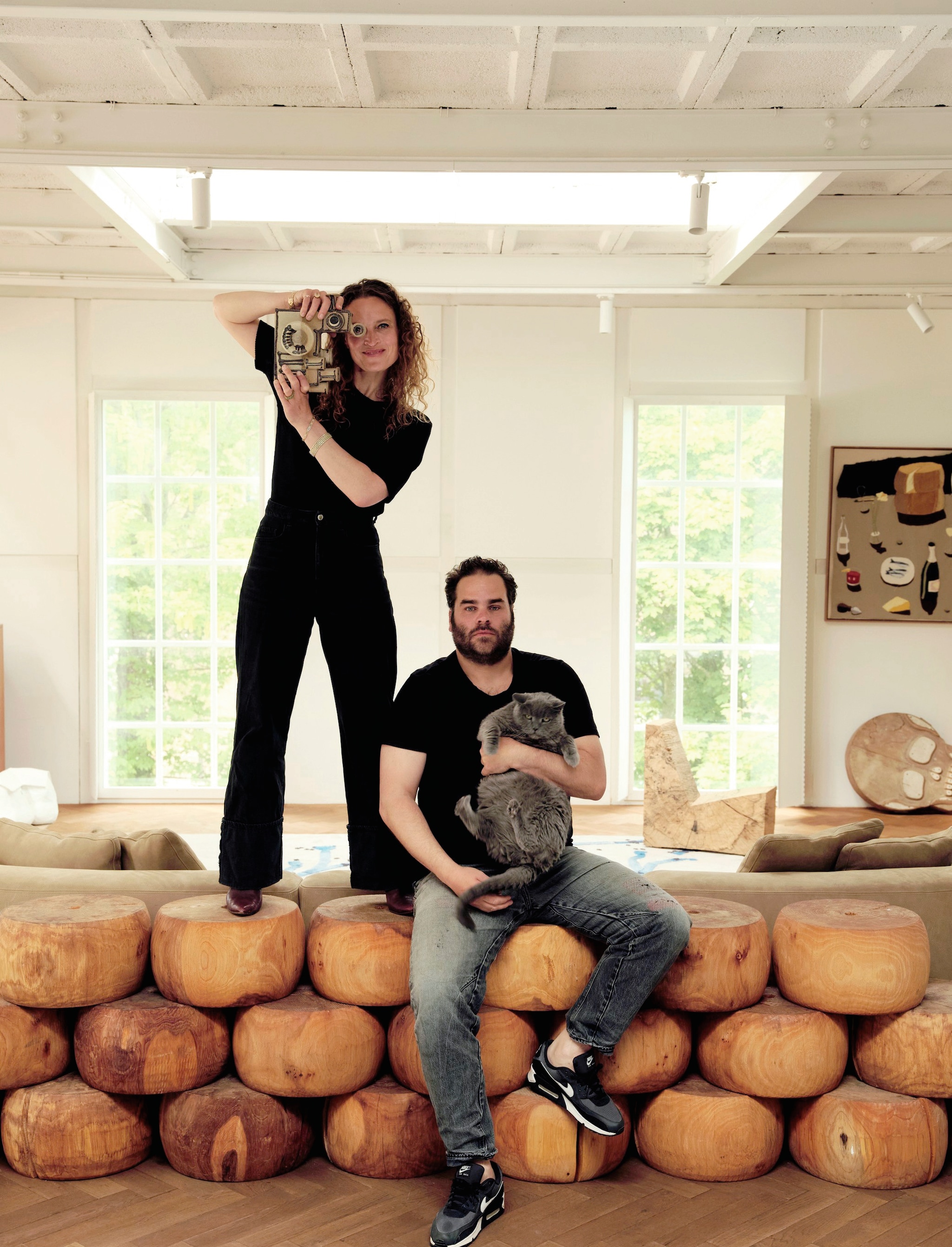 Esther, Frederik en kat Mus. Vintage camera van keramiek. Houten sculpturen Hacked Cheese Earthquake Tower van Studio Molen. Bank Piet Boon. Houten stoel Arne Kristian. Schilderij Andrew Pierce Scott.