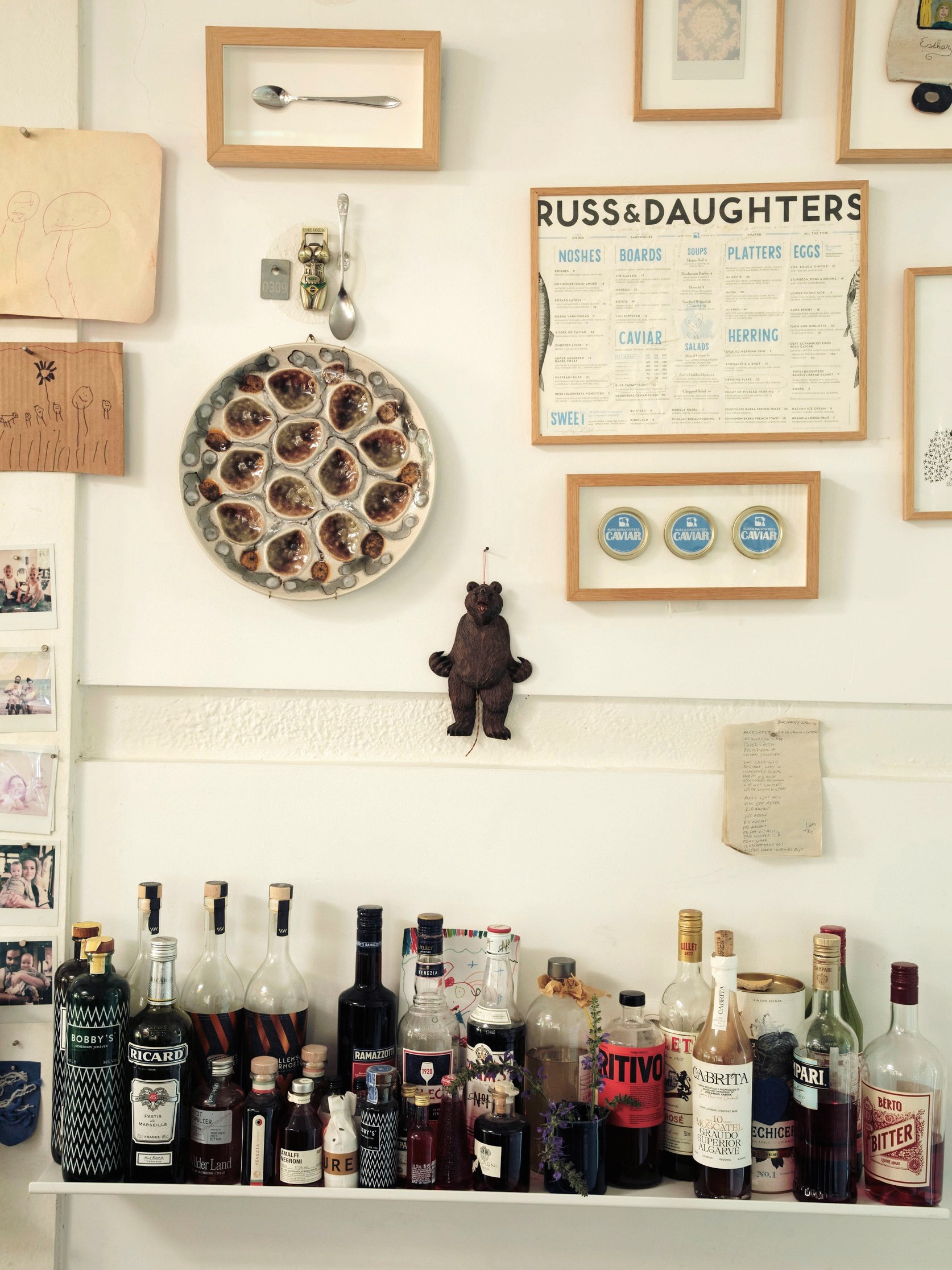 Wand met herinneringen van verschillende reizen. Ingelijst menu van Russ & Daughters. Afdruk van een rivierkreeft van restaurant Fred’s in Sydney. Frans oesterbord vintage. Tekening van dochter Rifka. vtwonen design 7-2026 | fotografie Oof Verschuren