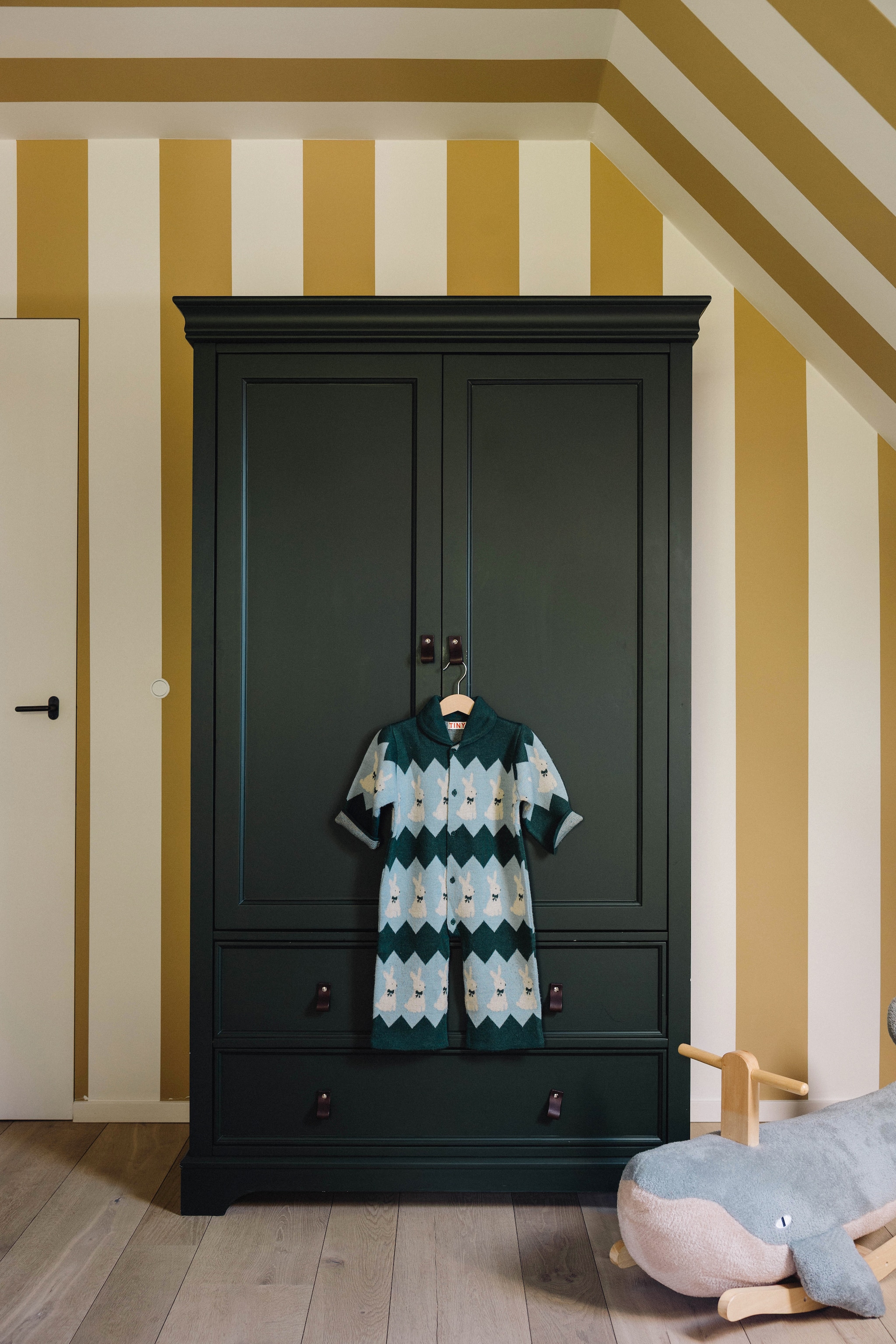 Blokstrepen op de muur geverfd met Keim Exclusiv 9317 en Sand van Farrow & Ball. Antieke kledingkast Uniques. Geverfd in kleur flessengroen Ral 6007. Hobbelwalvis Bloomingville. vtwonen Design 9-2026 | fotografie Stie De Neve