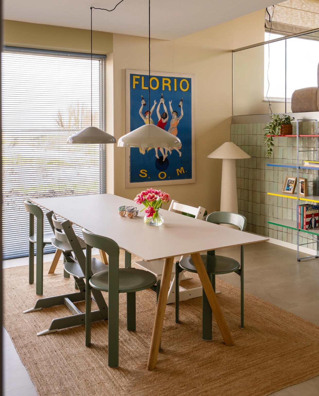 Tafel, stoelen en hanglampen Hay. Kinderstoelen Tripp Trapp van Stokke. Vloerkleed Zara Home. Kunstwerk Florio van Leonetto Cappiello via Werk aan de Muur. Staande lamp Kwantum. Tegels Platta Vert Clair via Designtegels. Aluminium jaloezieën Allure in Baby Blue van Veneta. Boekenkast Ikea. Muurkleur Wild Wonder van Flexa en Joa’s White van Farrow & Ball. Vloer Stanmore dryback beige van Floorlife.
 vtwonen 09-2026 | fotografie Lotte van Uittert