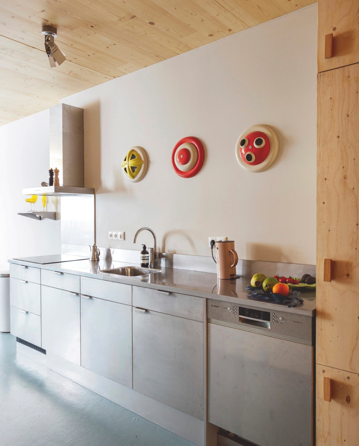 Vloer Paulycote kleur Sikkens Q8.15.55. Keuken afgewerkt met rvs. Wandobjecten Jeanine Eek-Keizer. Plafondspot Piet Hein Eek. Waterkoker Stelton. Peper- en zoutstel Le Creuset. Gieter Sekelskifte. vtwonen 10-2026 | styling Djolien De Kreij | fotografie Dana van Leeuwen